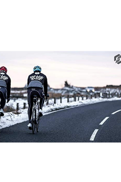 Two cyclists riding on an empty road with snow-covered fields