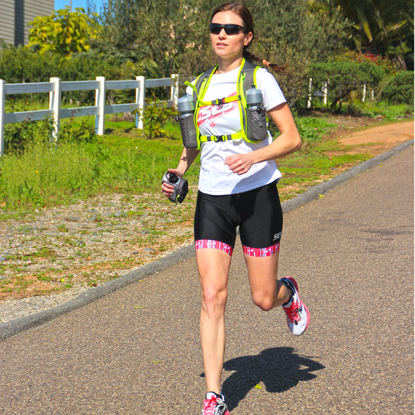 A person running on a road wearing a hydration vest with a handheld water bottle in hand