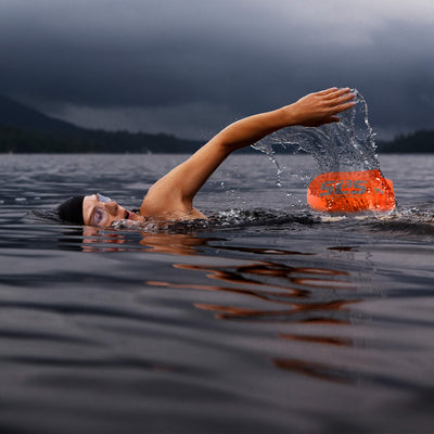 A person swimming in open water with an orange swim buoy